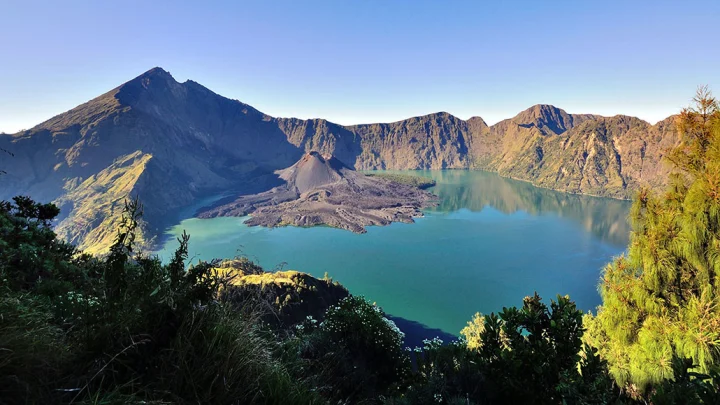 Vue panoramique du lac de caldeira Segara Anak sur le Mont Rinjani (Lombok), montrant le lac turquoise et le cône volcanique actif du Gunung Barujari émergeant de son centre, encadré par les crêtes escarpées