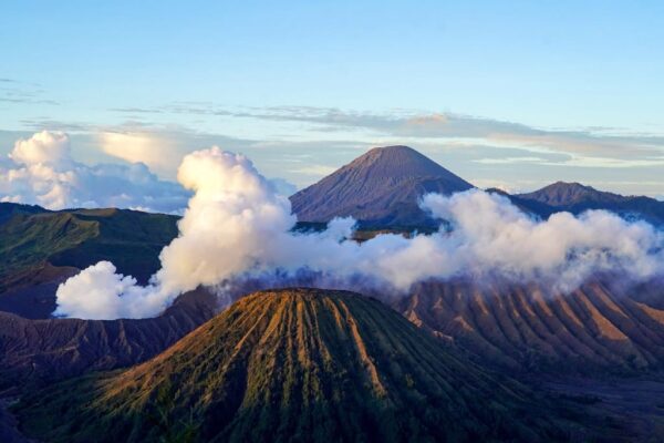 Sunrise view of Mount "Bromo" and other volcanic peaks in East Java, with white plumes of smoke rising from the crater.