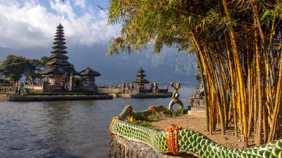 Le temple emblématique Pura Ulun Danu Beratan sur le lac Beratan à Bali, vu depuis la rive avec une balustrade en forme de dragon et des tiges de bambou au premier plan.