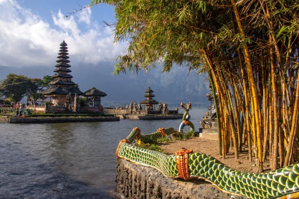 Le temple emblématique Pura Ulun Danu Beratan sur le lac Beratan à Bali, vu depuis la rive avec une balustrade en forme de dragon et des tiges de bambou au premier plan.