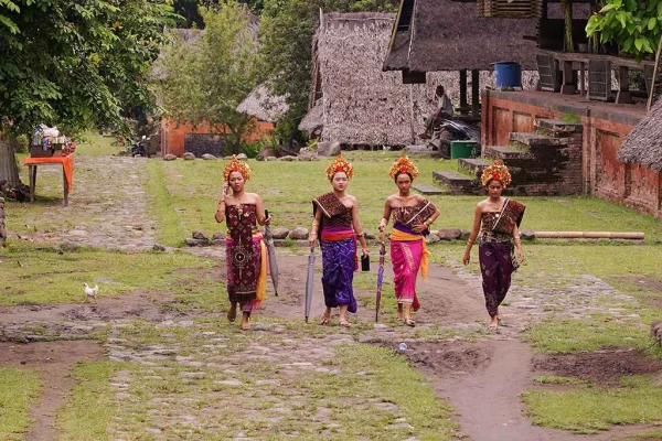 Group of women wearing vibrant traditional garments and ornate headwear walking through a rural village Tenganan, Bali